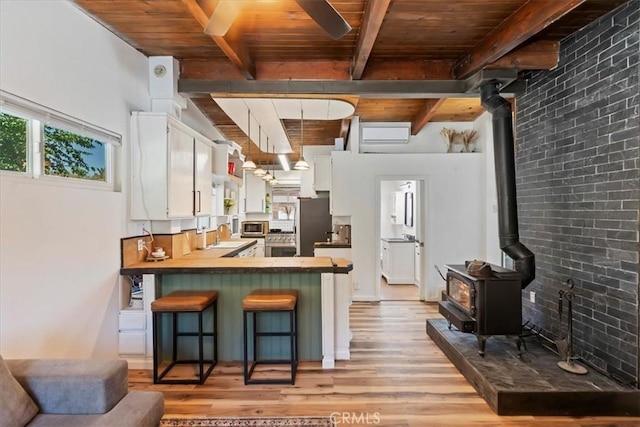 1946 Desert Front Rd, Wrightwood, CA 92397 - kitchen with a wood stove, a wooden ceiling with exposed beams, a peninsula, light wood finished floors, and white cabinetry