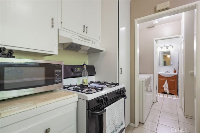 251 E Center St, Covina, CA 91723 - kitchen featuring white range with gas stovetop, under cabinet range hood, stainless steel microwave, tile countertops, and washer / clothes dryer