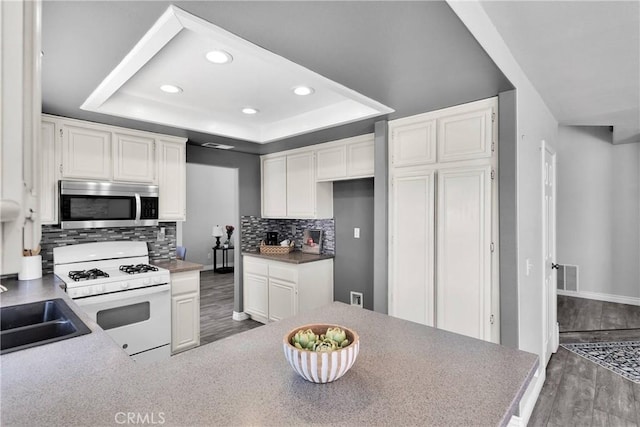 12725 Sundown Rd, Victorville, CA 92392 - kitchen featuring stainless steel microwave, white range with gas stovetop, a tray ceiling, dark wood-style flooring, and backsplash