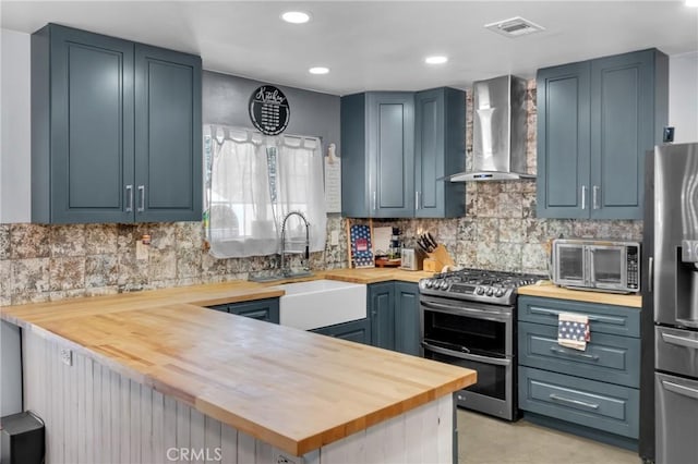 6320 Rancho Rio Rd, Paramount, CA 90723 - kitchen featuring wall chimney exhaust hood, butcher block countertops, appliances with stainless steel finishes, a peninsula, and decorative backsplash