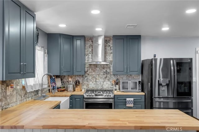 6320 Rancho Rio Rd, Paramount, CA 90723 - kitchen with wall chimney range hood, appliances with stainless steel finishes, backsplash, recessed lighting, and a peninsula