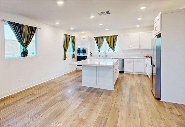 2750 W 182nd St Unit 112, Torrance, CA 90504 - kitchen with appliances with stainless steel finishes, light countertops, white cabinetry, a kitchen island, and light wood-style floors