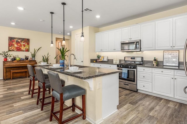2910 Lucia Jade Loop, San Diego, CA 92139 - kitchen with stainless steel appliances, light wood-style floors, white cabinets, a breakfast bar, and a center island with sink