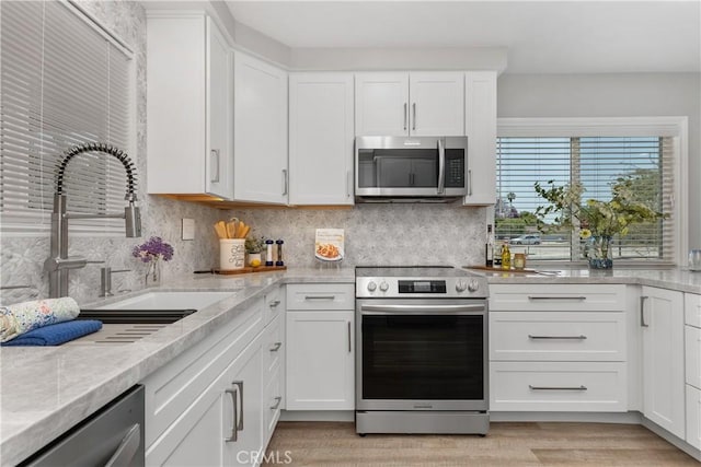1837 N Studebaker Rd, Long Beach, CA 90815 - kitchen featuring stainless steel appliances, white cabinetry, decorative backsplash, and light wood-type flooring