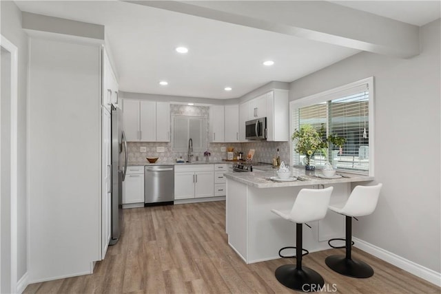 1837 N Studebaker Rd, Long Beach, CA 90815 - kitchen with stainless steel appliances, a peninsula, light wood-style flooring, tasteful backsplash, and white cabinetry