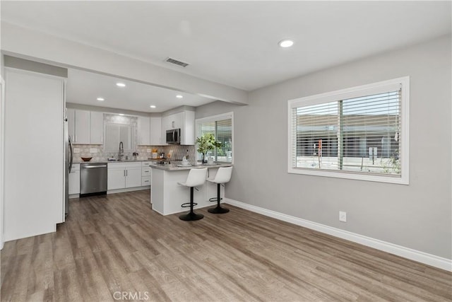 1837 N Studebaker Rd, Long Beach, CA 90815 - kitchen with stainless steel appliances, a peninsula, a kitchen bar, wood finished floors, and white cabinets