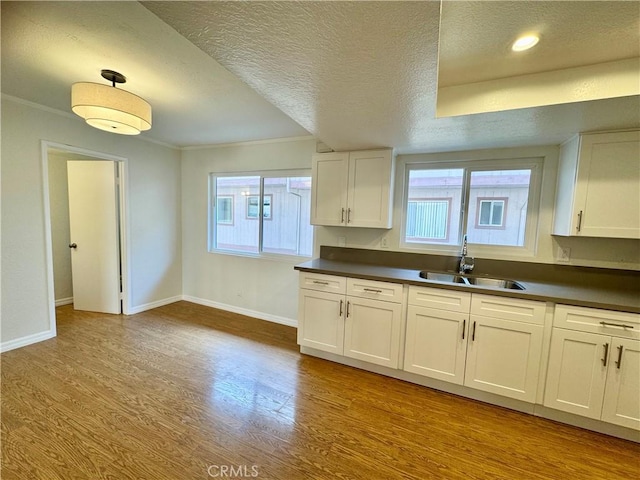 9010 Burke St Unit 22, Pico Rivera, CA 90660 - kitchen featuring ornamental molding, a textured ceiling, dark countertops, wood finished floors, and white cabinetry