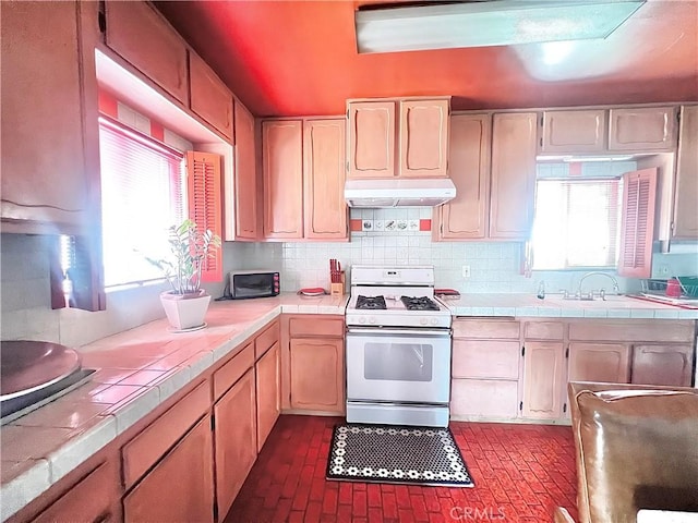 407 S Northwood Ave, Compton, CA 90220 - kitchen featuring white range with gas cooktop, tile counters, under cabinet range hood, backsplash, and brick patterned floors
