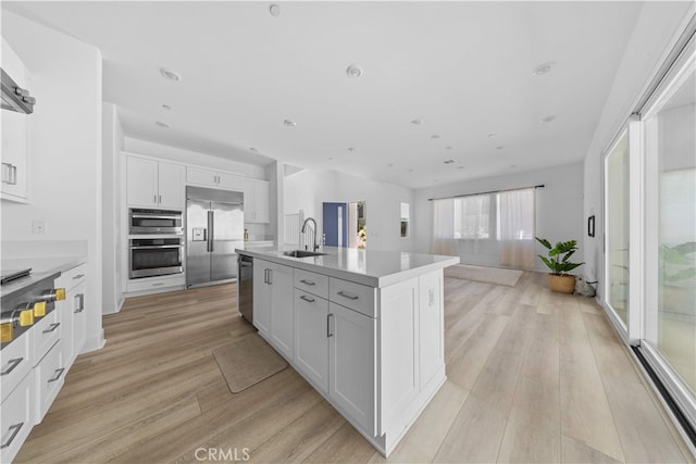 27216 W Coyote Bush Ct, Valencia, CA 91355 - kitchen with stainless steel appliances, light wood-style floors, a kitchen island with sink, white cabinets, and open floor plan