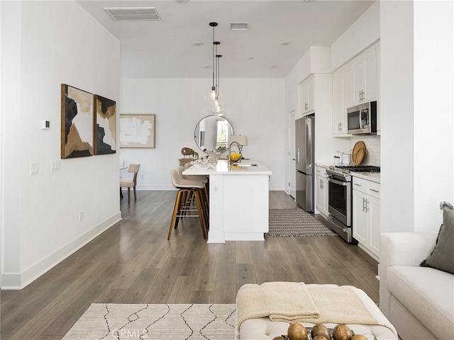 1673 Lexington Ln, San Pedro, CA 90732 - kitchen featuring appliances with stainless steel finishes, an island with sink, white cabinetry, and dark wood-type flooring