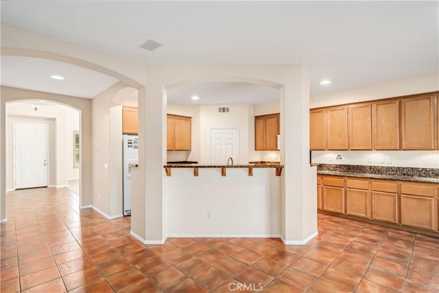 40028 Bluff Ct, Palmdale, CA 93551 - kitchen featuring recessed lighting, white refrigerator with ice dispenser, arched walkways, light tile patterned floors, and dark stone counters