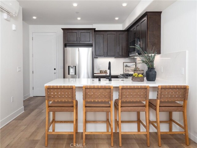 402 W Grand Ave Unit 101, Grover Beach, CA 93433 - kitchen featuring appliances with stainless steel finishes, a peninsula, light wood finished floors, dark brown cabinets, and a wall mounted AC