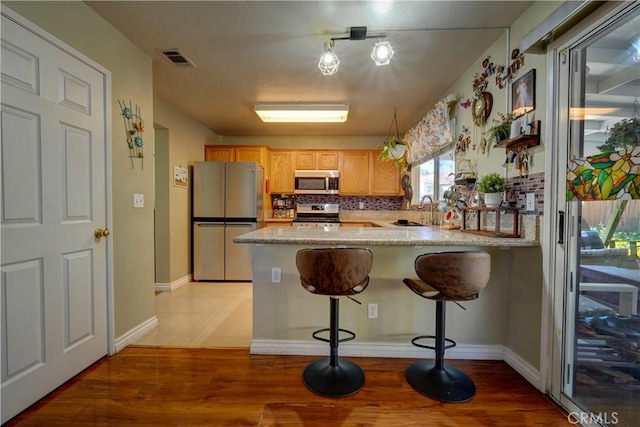 1808 Cave St, Redlands, CA 92374 - kitchen with appliances with stainless steel finishes, a peninsula, tasteful backsplash, a breakfast bar, and light wood-style flooring