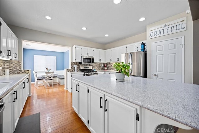 17733 Willow Dr, Riverside, CA 92503 - kitchen featuring appliances with stainless steel finishes, backsplash, white cabinets, light wood-style floors, and light stone counters