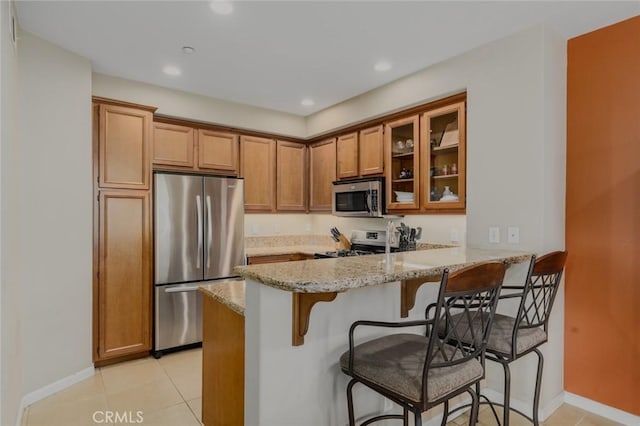 8036 Picasso, Stanton, CA 90680 - kitchen with stainless steel appliances, brown cabinets, a peninsula, a breakfast bar, and light stone countertops