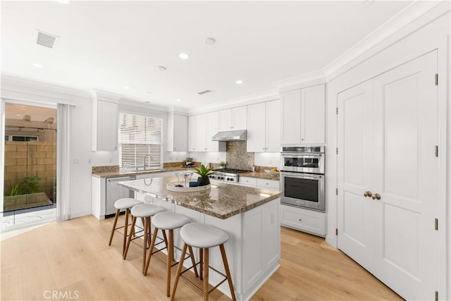 112 Velvet Leaf, Irvine, CA 92620 - kitchen with appliances with stainless steel finishes, a breakfast bar area, white cabinetry, light wood finished floors, and crown molding