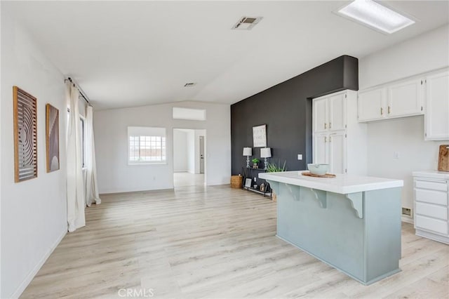 13432 Jubilee Pl, Victorville, CA 92395 - kitchen featuring vaulted ceiling, white cabinets, light countertops, light wood-style flooring, and a kitchen breakfast bar
