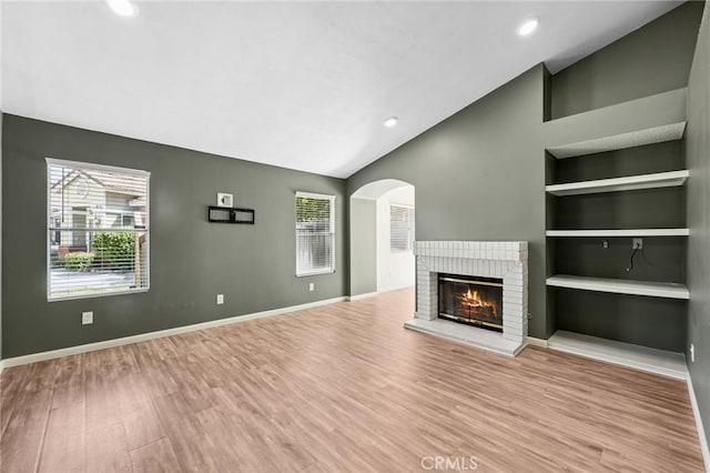 1422 Deborah Pl, Beaumont, CA 92223 - unfurnished living room with lofted ceiling, built in shelves, a brick fireplace, wood finished floors, and arched walkways