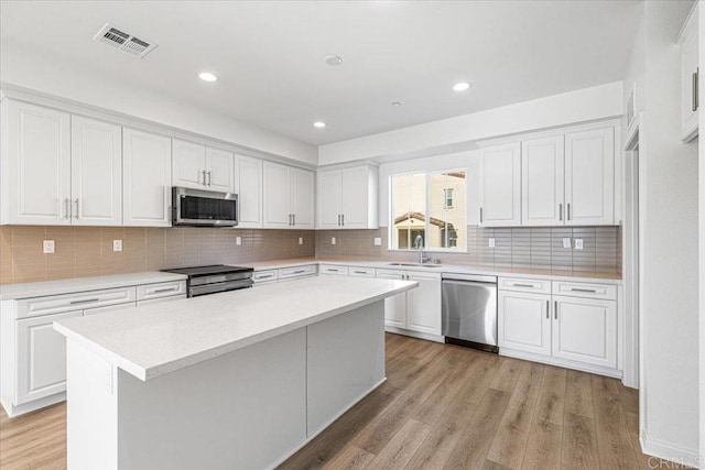 8608 Amherst St, Santee, CA 92071 - kitchen featuring stainless steel appliances, white cabinets, light wood finished floors, light countertops, and decorative backsplash