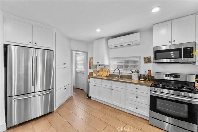 606 N Bonnie Brae St, Los Angeles, CA 90026 - kitchen featuring appliances with stainless steel finishes, a wall mounted AC, light tile patterned floors, white cabinets, and recessed lighting