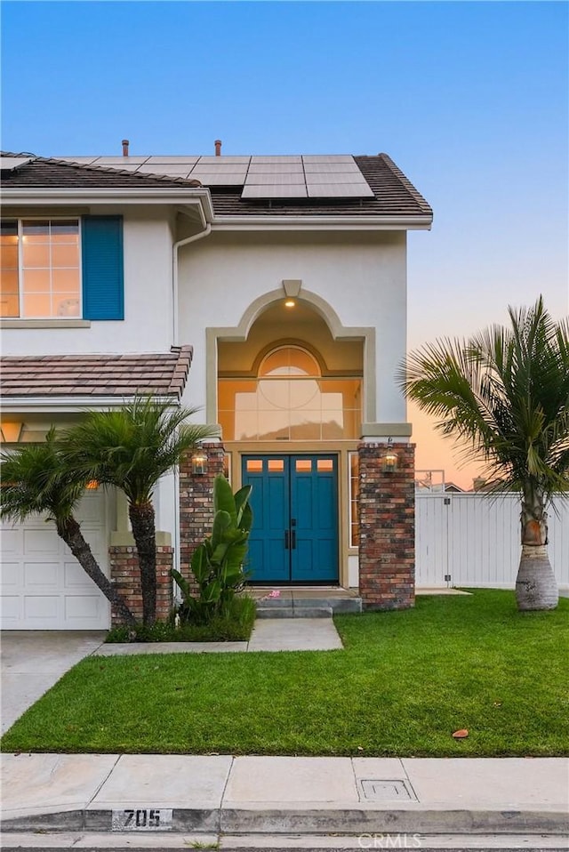 705 El Berro, San Clemente, CA 92672 - view of exterior entry with stucco siding, a lawn, roof mounted solar panels, an attached garage, and concrete driveway