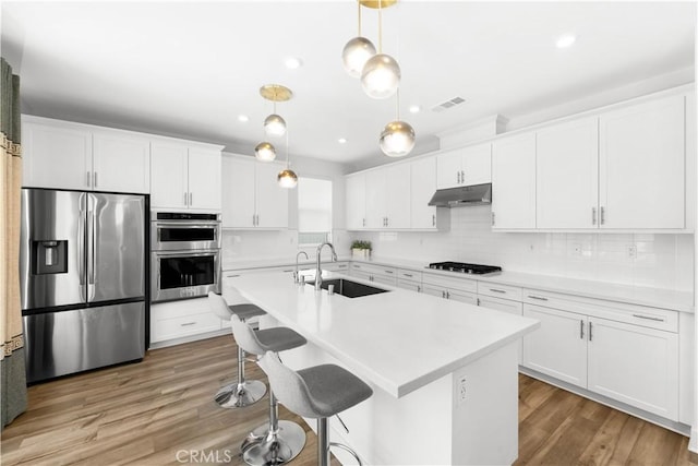 16526 Trailblazer Ave, Chino, CA 91708 - kitchen featuring appliances with stainless steel finishes, under cabinet range hood, white cabinets, light countertops, and a center island with sink