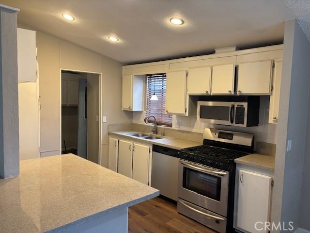 10450 Stageline St, Corona, CA 92883 - kitchen with stainless steel appliances, dark wood-style flooring, white cabinets, lofted ceiling, and light countertops