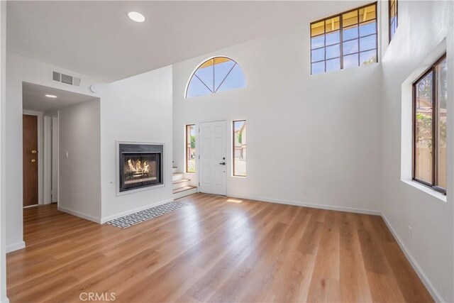 8939 Gallatin Rd Unit 68, Pico Rivera, CA 90660 - unfurnished living room with light wood-style floors, a glass covered fireplace, recessed lighting, and a towering ceiling