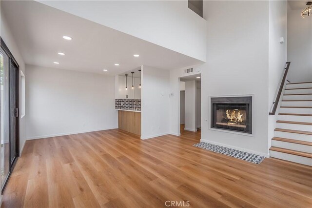 8939 Gallatin Rd Unit 68, Pico Rivera, CA 90660 - unfurnished living room with a lit fireplace, light wood finished floors, recessed lighting, and stairs