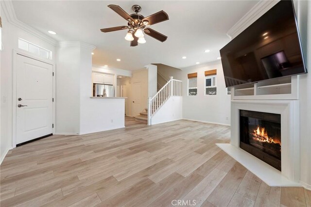72 Westwind Dr, Tustin, CA 92782 - unfurnished living room featuring ornamental molding, stairs, a ceiling fan, light wood-style flooring, and a glass covered fireplace