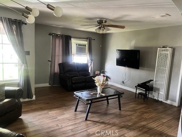 1550 W 21st St, San Bernardino, CA 92411 - living area featuring a heating unit, a wall mounted air conditioner, ceiling fan, and dark wood-style floors