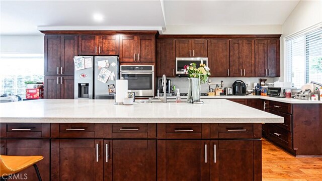 937 Dahlia Ave, Costa Mesa, CA 92626 - kitchen with appliances with stainless steel finishes, light wood-type flooring, a large island, dark brown cabinetry, and light stone countertops