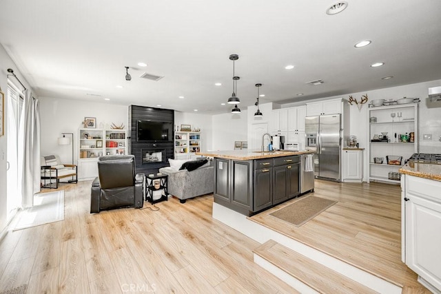 25252 Atwood Blvd, Newhall, CA 91321 - kitchen with appliances with stainless steel finishes, white cabinets, light wood finished floors, an island with sink, and a large fireplace