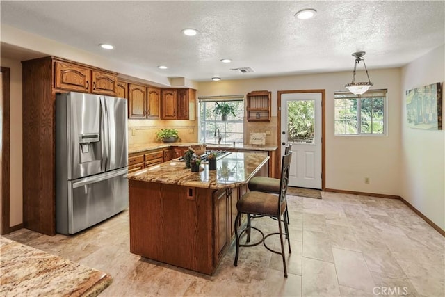 18836 Cedar Valley Way, Newhall, CA 91321 - kitchen with stainless steel fridge with ice dispenser, light stone countertops, decorative backsplash, a kitchen breakfast bar, and brown cabinets