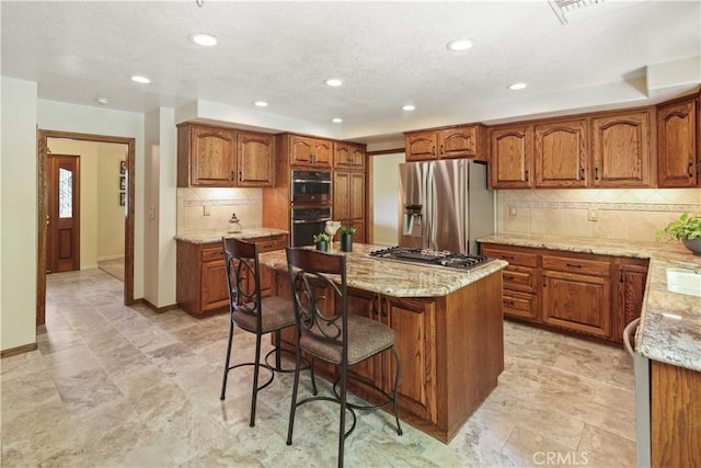 18836 Cedar Valley Way, Newhall, CA 91321 - kitchen featuring appliances with stainless steel finishes, brown cabinets, light stone counters, decorative backsplash, and a kitchen island