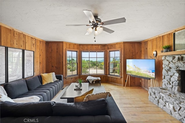 10821 Los Jordans Rd, Agua Dulce, CA 91390 - living area featuring light wood-style flooring, wood walls, a ceiling fan, a textured ceiling, and a stone fireplace