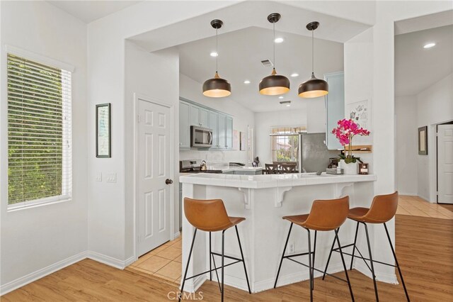 80848 Sunspring Ct, Indio, CA 92201 - kitchen with stainless steel appliances, tile countertops, a kitchen breakfast bar, a peninsula, and light wood-style floors