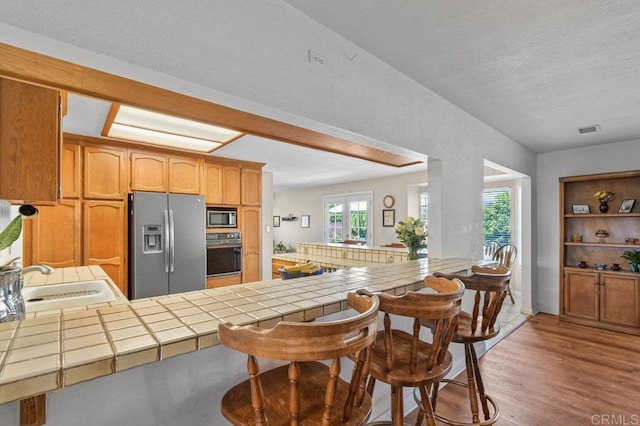 5855 Kappa St, La Mesa, CA 91942 - kitchen with stainless steel appliances, tile countertops, light wood-type flooring, a peninsula, and a kitchen bar