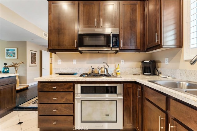 4424 Whitsett Ave Unit 312, Studio City, CA 91604 - kitchen featuring appliances with stainless steel finishes, dark brown cabinetry, light tile patterned floors, and light stone countertops