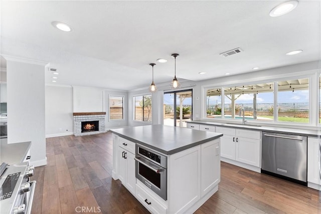 28422 La Pradera, Laguna Niguel, CA 92677 - kitchen with appliances with stainless steel finishes, white cabinetry, dark countertops, a fireplace, and dark wood-style flooring