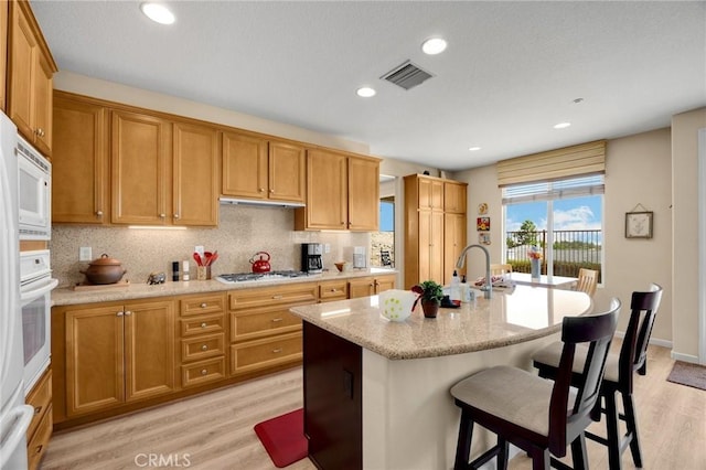 3667 Skylark Way, Brea, CA 92823 - kitchen featuring light wood-style floors, tasteful backsplash, a kitchen breakfast bar, a kitchen island with sink, and light stone counters