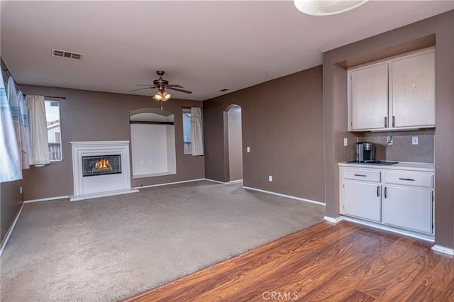25540 Riley Cir, Menifee, CA 92585 - unfurnished living room with ceiling fan, arched walkways, a glass covered fireplace, wood finished floors, and carpet floors