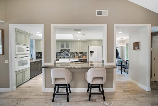 24532 Moonfire Dr, Dana Point, CA 92629 - kitchen with white appliances, light wood finished floors, backsplash, a breakfast bar, and recessed lighting