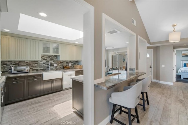 24532 Moonfire Dr, Dana Point, CA 92629 - kitchen featuring dishwasher, a breakfast bar area, light wood-style flooring, decorative backsplash, and vaulted ceiling