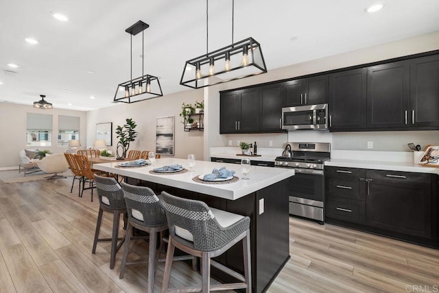 3510 Brody Way, Oceanside, CA 92056 - kitchen with appliances with stainless steel finishes, dark cabinets, light countertops, a kitchen bar, and light wood-type flooring