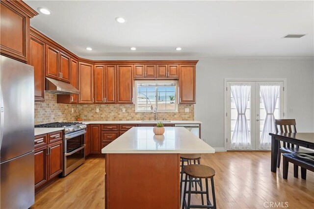 18651 E Weather Rd, Covina, CA 91722 - kitchen with appliances with stainless steel finishes, under cabinet range hood, a breakfast bar, light countertops, and light wood-style flooring