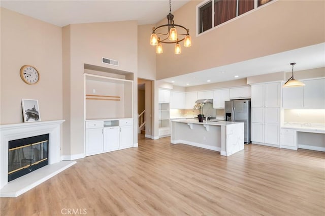13711 Hidden, Eastvale, CA 92880 - unfurnished living room featuring light wood finished floors, a chandelier, high vaulted ceiling, stairs, and a glass covered fireplace
