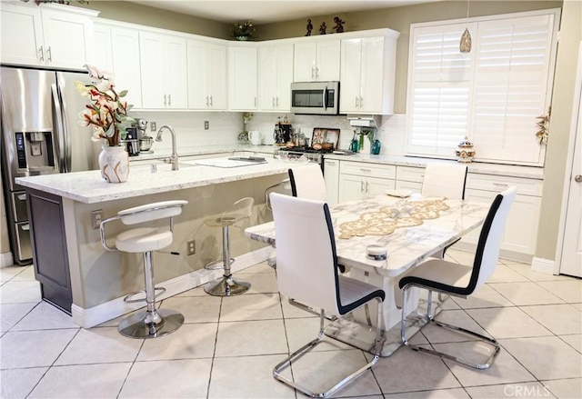 12170 Orgren Ave, Chino, CA 91710 - kitchen with stainless steel appliances, a kitchen island with sink, a breakfast bar area, white cabinets, and light stone counters