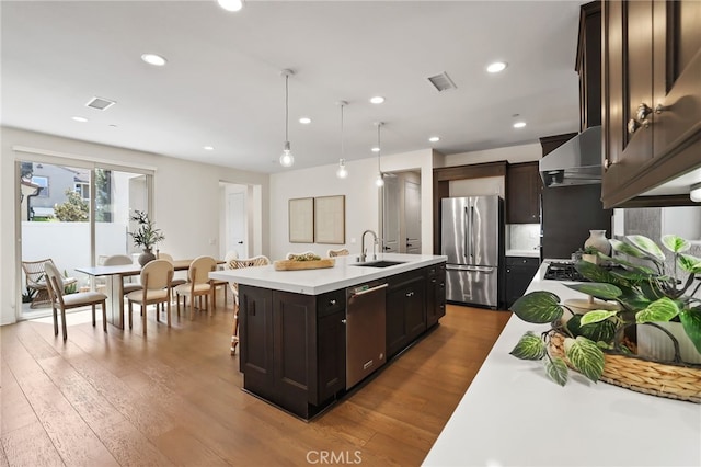 143 Hollow Tree, Irvine, CA 92618 - kitchen with stainless steel appliances, light countertops, dark wood-style flooring, a kitchen island with sink, and wall chimney range hood