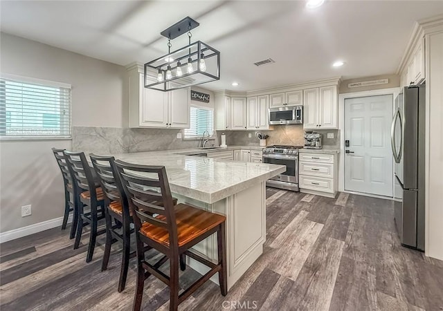 2288 Marilyn St, Simi Valley, CA 93065 - kitchen featuring appliances with stainless steel finishes, a peninsula, dark wood-type flooring, tasteful backsplash, and a breakfast bar area
